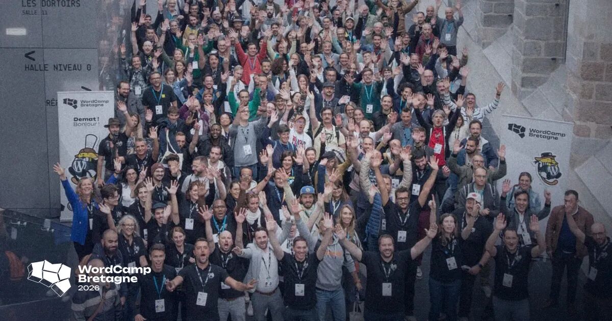 Photo de groupe des participants du WordCamp Bretagne, bras levés dans le hall du Couvent des Jacobins à Rennes, devant les kakémonos de l'événement